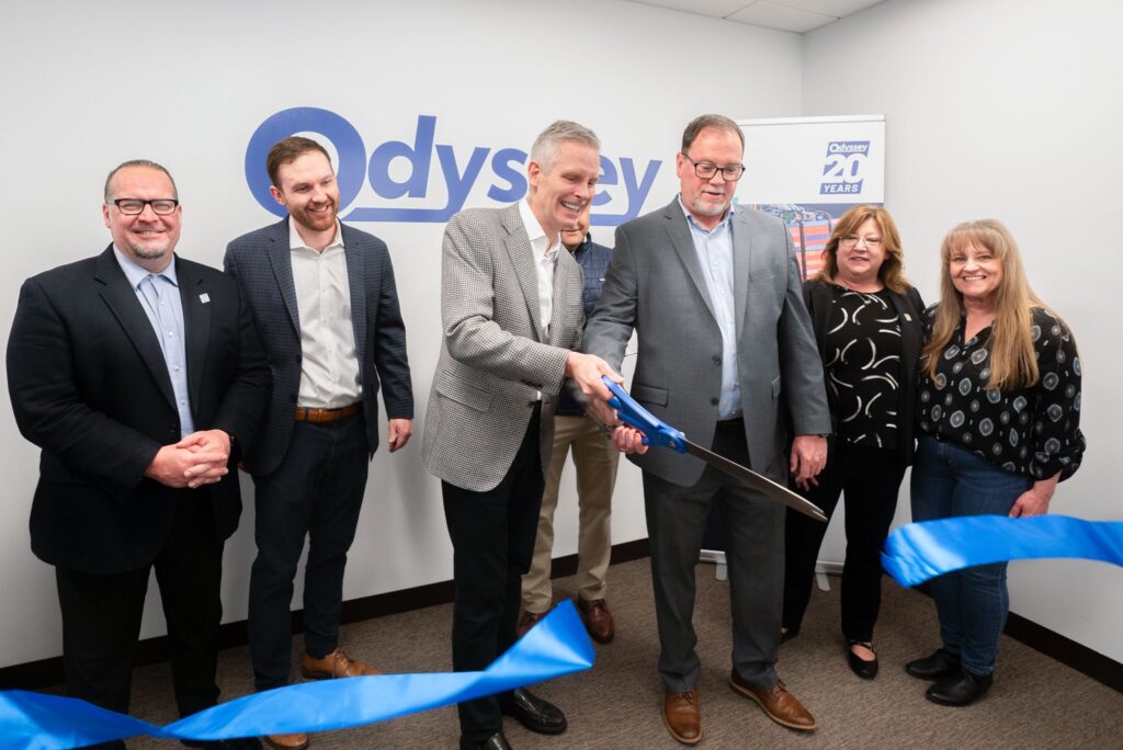 Odyssey employees standing next to each other as Hans cuts a blue ribbon in half with giant scissors