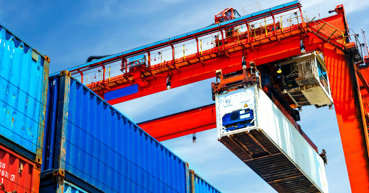shipping containers being moved around a shipping port by a crane